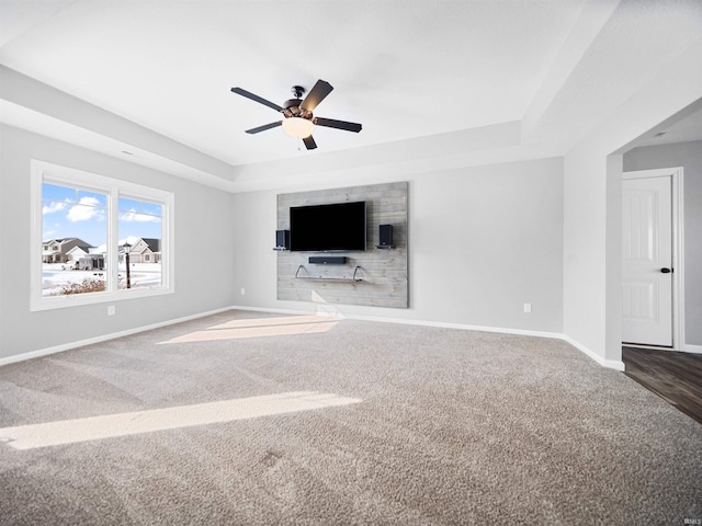 unfurnished living room with carpet, baseboards, a raised ceiling, and a ceiling fan