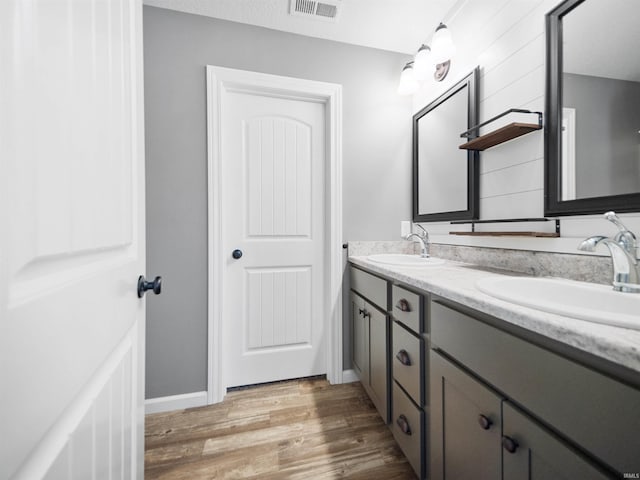 bathroom featuring double vanity, visible vents, a sink, and wood finished floors