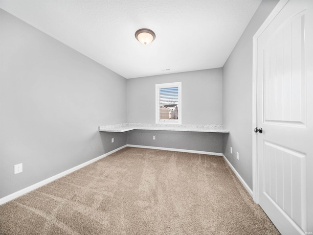 carpeted empty room with baseboards and built in study area