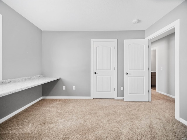 unfurnished bedroom featuring carpet, built in study area, and baseboards