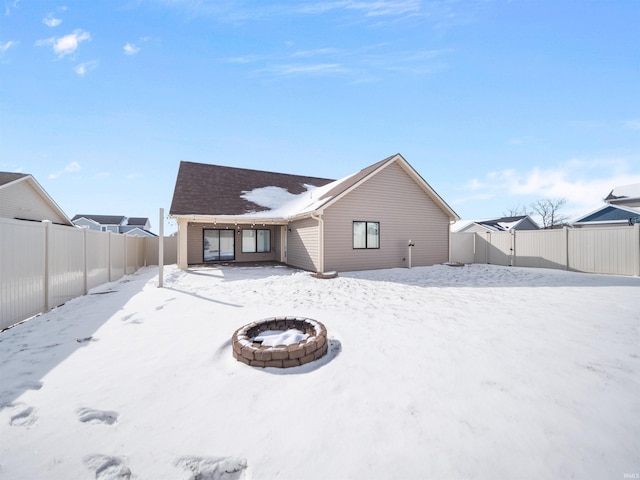 snow covered rear of property featuring a fenced backyard and a fire pit