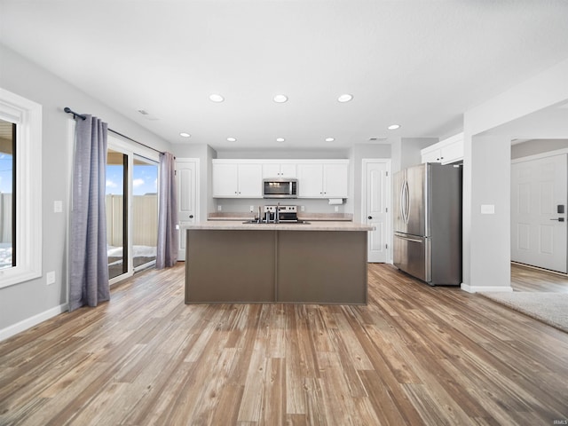 kitchen featuring stainless steel appliances, light countertops, light wood-style flooring, white cabinets, and an island with sink