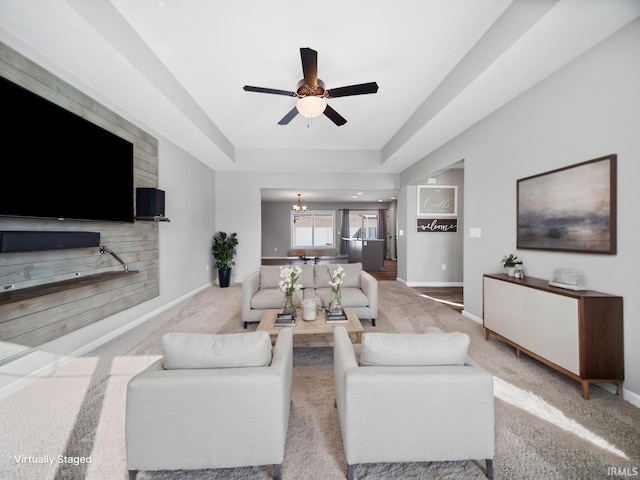 living area featuring ceiling fan with notable chandelier, a tray ceiling, carpet flooring, and baseboards