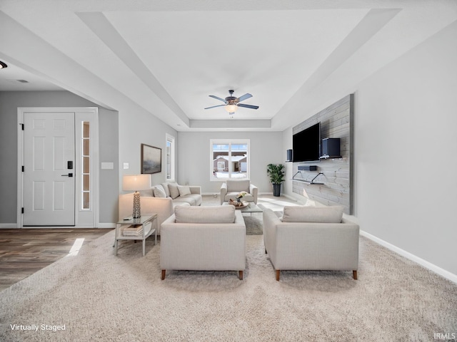 living room featuring ceiling fan, baseboards, and a raised ceiling