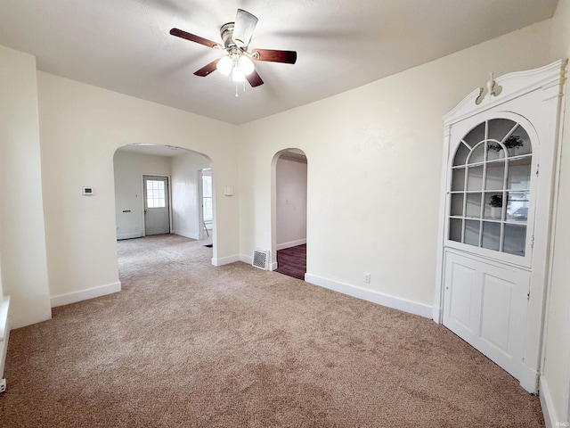 carpeted empty room featuring baseboards, visible vents, arched walkways, and a ceiling fan