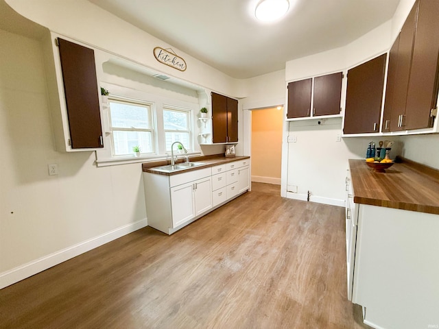 kitchen with baseboards, butcher block countertops, light wood-type flooring, open shelves, and a sink