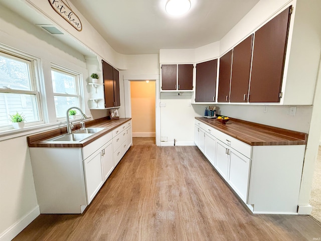 kitchen featuring open shelves, light wood finished floors, a sink, and baseboards