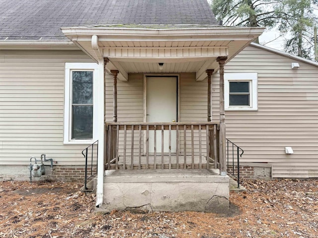 entrance to property featuring a porch and a shingled roof