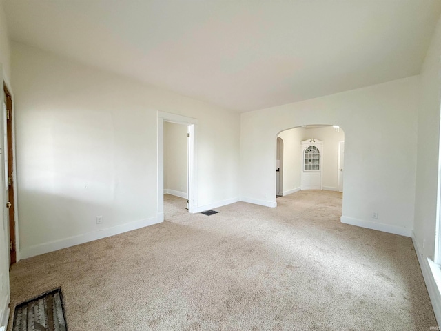 unfurnished room with baseboards, visible vents, arched walkways, and light colored carpet