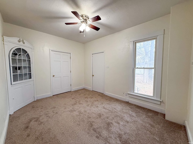 unfurnished bedroom featuring a ceiling fan, carpet, multiple windows, and baseboards