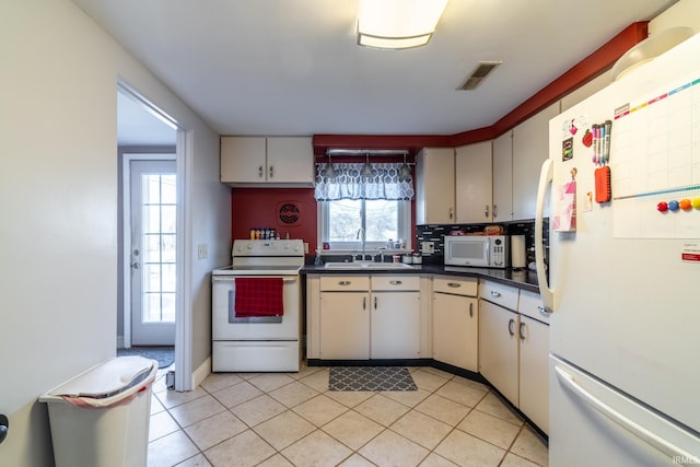 kitchen featuring dark countertops, visible vents, backsplash, a sink, and white appliances