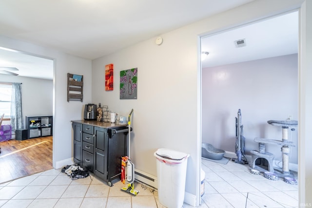 interior space featuring light tile patterned floors, visible vents, a baseboard heating unit, and baseboards