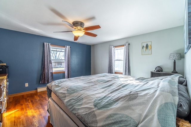 bedroom with dark wood-type flooring, multiple windows, a baseboard radiator, and baseboards