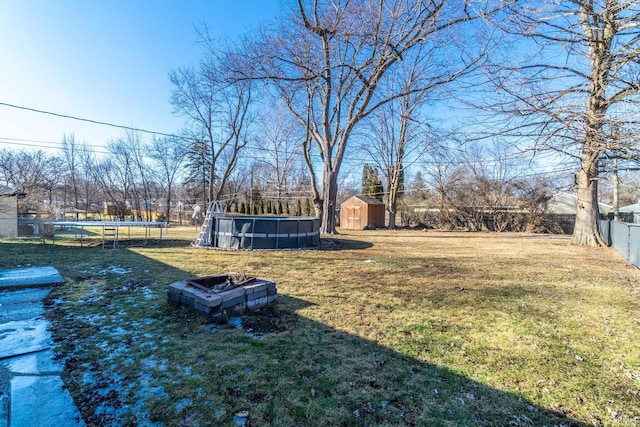 view of yard with an outdoor fire pit, fence, an outdoor pool, a storage unit, and a trampoline