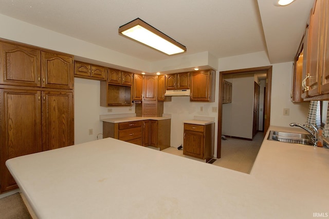 kitchen with a peninsula, under cabinet range hood, brown cabinetry, and a sink