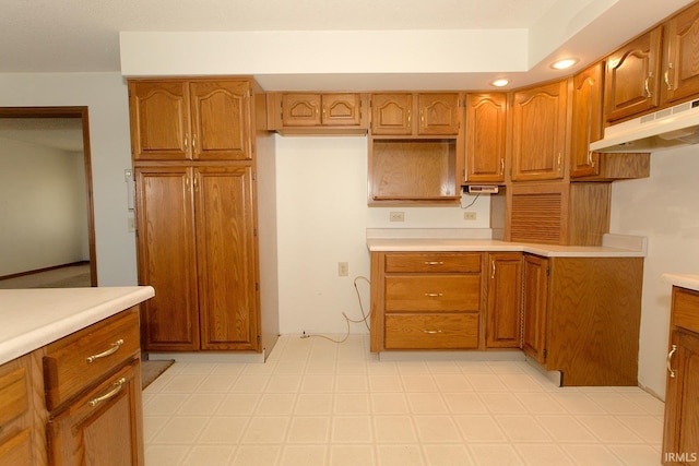 kitchen featuring under cabinet range hood, brown cabinetry, and light floors