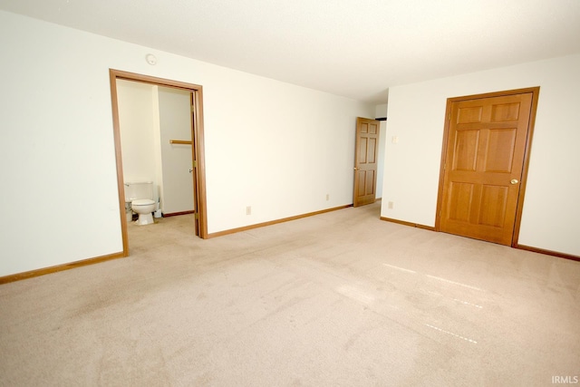 unfurnished bedroom with light colored carpet, connected bathroom, and baseboards