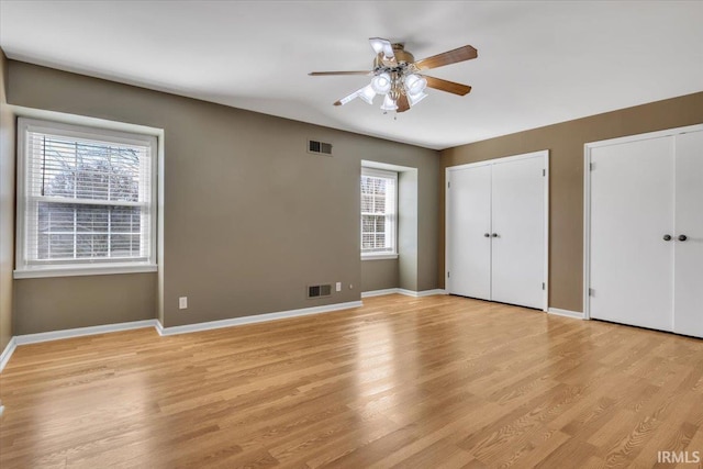 unfurnished bedroom with baseboards, light wood-style flooring, visible vents, and multiple closets