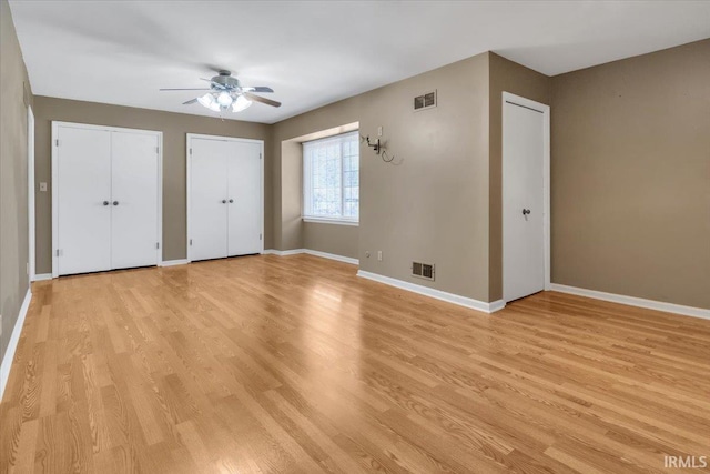 unfurnished bedroom featuring multiple closets, visible vents, light wood-style flooring, and baseboards