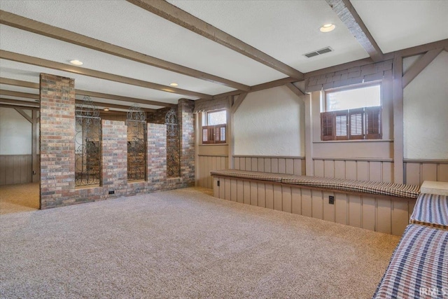 interior space with a wainscoted wall, carpet floors, a textured ceiling, and visible vents