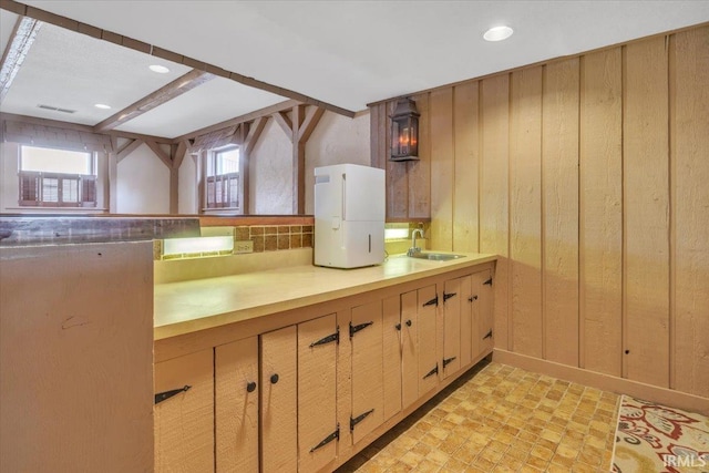 kitchen with wood walls, light countertops, a sink, and light floors