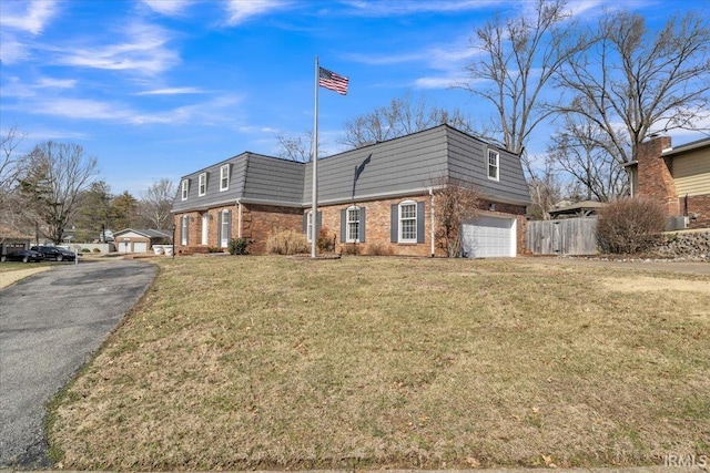 view of front of home with mansard roof, a front yard, fence, and brick siding