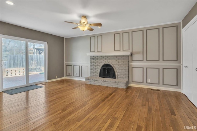 unfurnished living room featuring a brick fireplace, a ceiling fan, a decorative wall, and hardwood / wood-style floors