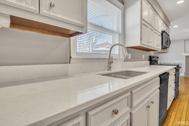 kitchen with light wood finished floors, recessed lighting, white cabinets, a sink, and black appliances