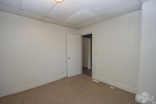 empty room with baseboards, visible vents, a drop ceiling, and carpet flooring