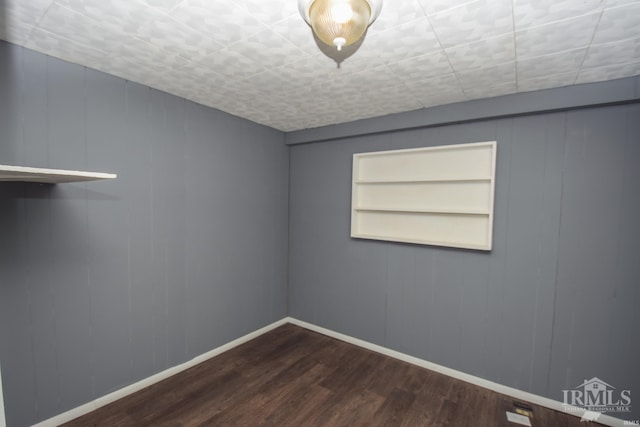 unfurnished room with baseboards, built in features, and dark wood finished floors