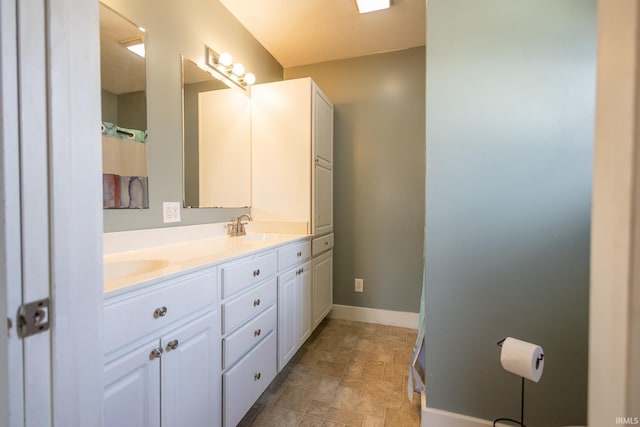 full bathroom with double vanity, stone finish flooring, baseboards, and a sink