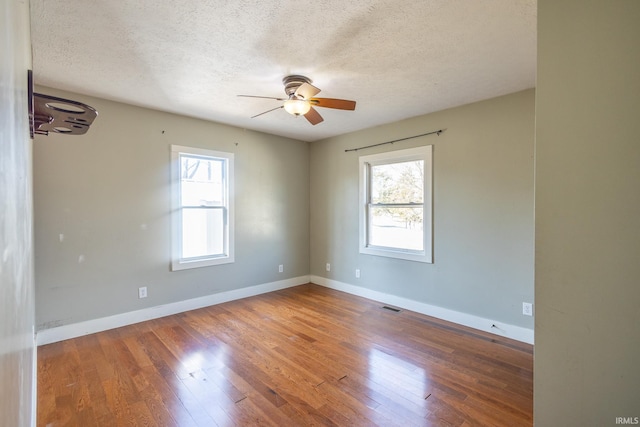 spare room with a wealth of natural light, wood-type flooring, visible vents, and baseboards