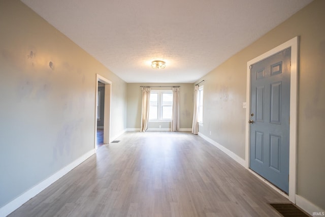 spare room with visible vents, a textured ceiling, baseboards, and wood finished floors