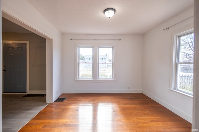 empty room featuring light wood-type flooring, a healthy amount of sunlight, baseboards, and visible vents