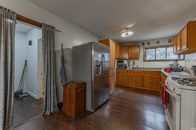 kitchen featuring white range with gas stovetop, dark wood finished floors, brown cabinets, stainless steel refrigerator with ice dispenser, and a sink