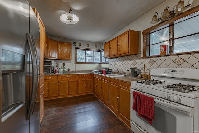 kitchen featuring dark wood-type flooring, a sink, fridge with ice dispenser, brown cabinets, and gas range gas stove