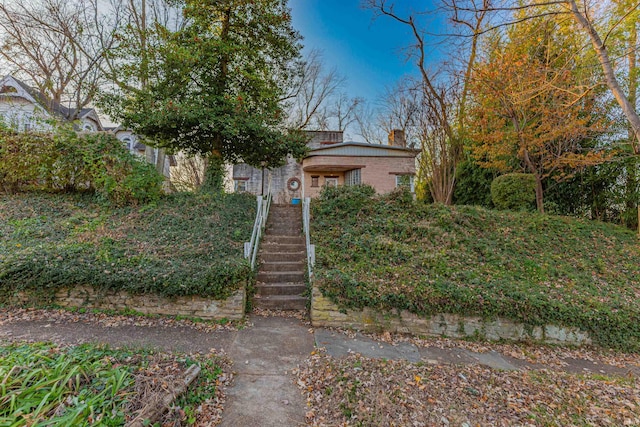 view of front facade with stairway, brick siding, and a chimney