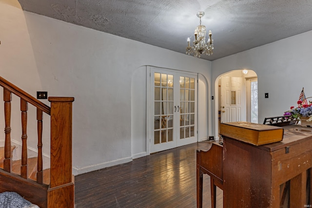 interior space featuring baseboards, arched walkways, wood finished floors, an inviting chandelier, and french doors