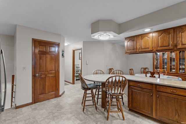 kitchen featuring a breakfast bar area, brown cabinets, baseboards, and light stone countertops