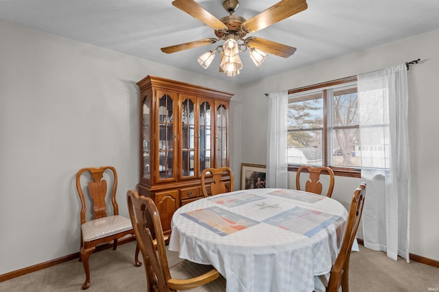 dining space with a ceiling fan, light carpet, and baseboards