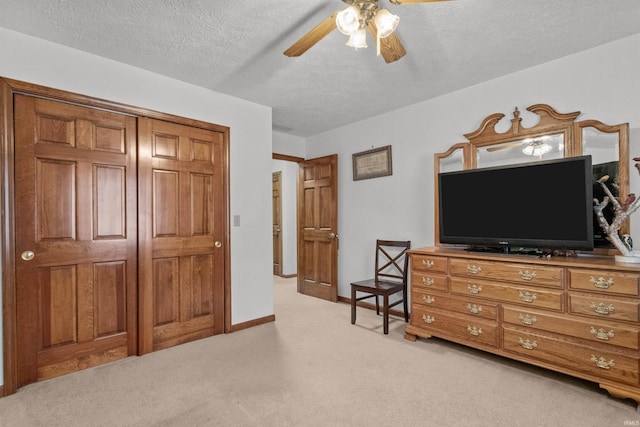 bedroom with a closet, light colored carpet, ceiling fan, a textured ceiling, and baseboards