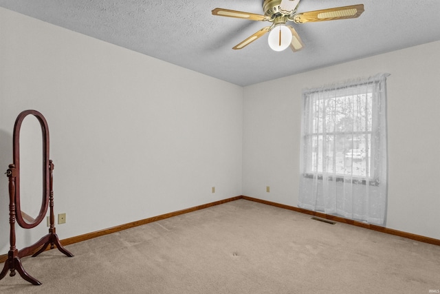 carpeted spare room with a ceiling fan, visible vents, a textured ceiling, and baseboards