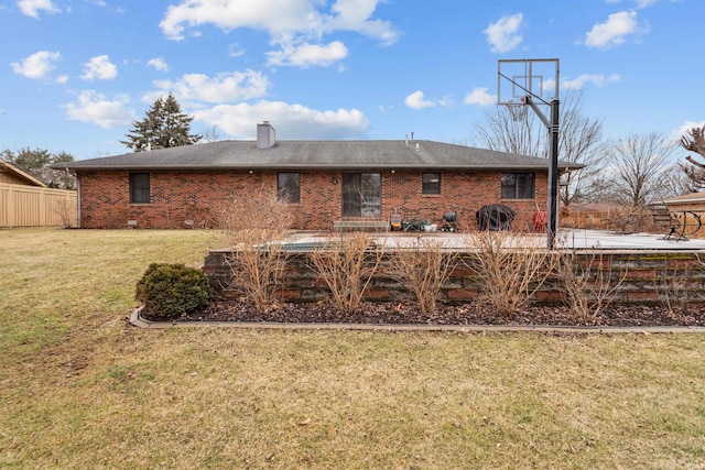 rear view of house featuring a yard, a chimney, fence, and brick siding