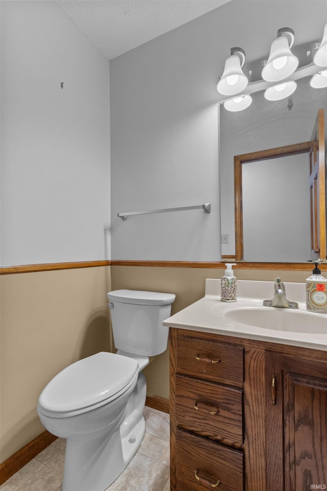 half bathroom with toilet, a textured ceiling, vanity, baseboards, and tile patterned floors