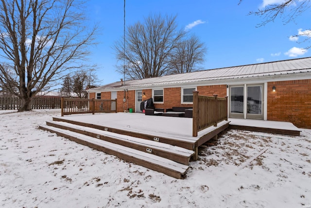 snow covered rear of property with metal roof, fence, a deck, and brick siding