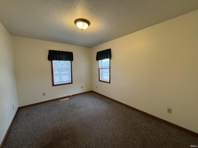 unfurnished room featuring baseboards, visible vents, dark colored carpet, and a textured ceiling