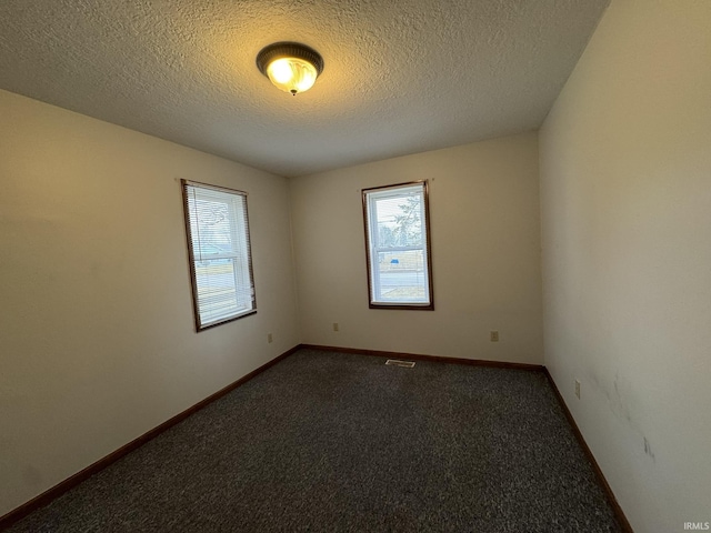 unfurnished room with visible vents, dark carpet, a textured ceiling, and baseboards