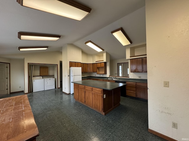 kitchen featuring dark floors, a kitchen island, independent washer and dryer, freestanding refrigerator, and dark countertops