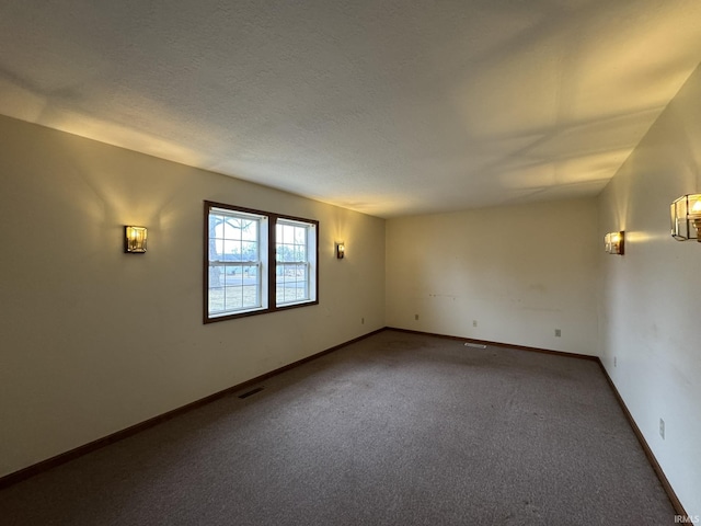 spare room with a textured ceiling, carpet flooring, visible vents, and baseboards