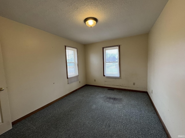 empty room featuring a textured ceiling, carpet floors, visible vents, and baseboards